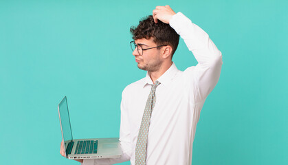 businessman with laptop feeling puzzled and confused, scratching head and looking to the side