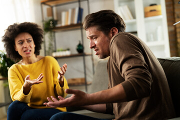 Frustrated young couple arguing at home. Stressed unhappy wife and husband sitting on cauch at home..