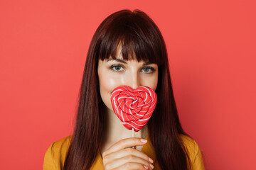 Close up studio shot of charming young red haired woman, wearing yellow shirt, holding a heart...