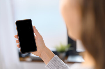 Back view at an empty smartphone screen in hand of a woman, woman holds a mobile phone with blank display, mockup, copy space