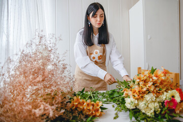 a young brunette woman in an apron in the process of creating a bouquet in the rustic style in her flower shop