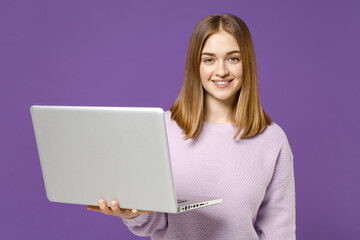 Young smiling positive happy freelancer student caucasian woman wear purple knitted sweater using laptop pc computer chatting isolated on violet background studio portrait People lifestyle concept