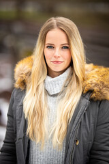 Portrait of a blonde girl with an anorak and fur collar smiling at the camera, in the background railroad tracks in the blur..