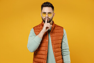 Young secret caucasian man 20s wear orange vest mint sweatshirt glasses saying hush be quiet with...