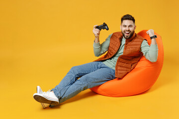 Full length young excited man 20s in orange vest mint sweatshirt sitting in beanbag bag chair...