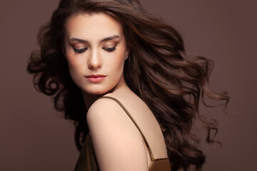 Portrait of young pretty woman brunette with dark blowing curly hair and clear healthy skin on brown background