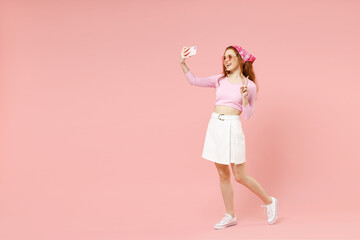 Fun young friendly happy woman in rose clothes bandana glasses do selfie shot on mobile phone show v-sign victory gesture isolated on pastel pink background studio portrait People lifestyle concept