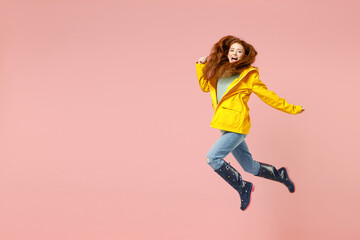 Fototapeta na wymiar Full length side view redhead excited young woman in yellow waterproof raincoat outerwear jump high run fast isolated on pastel pink background studio Outdoor lifestyle fall weather season concept