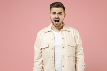 Young shocked amazed surprised impressed trendy caucasian man 20s in jacket white t-shirt looking camera with opened mouth isolated on pastel pink background studio portrait. People lifestyle concept.