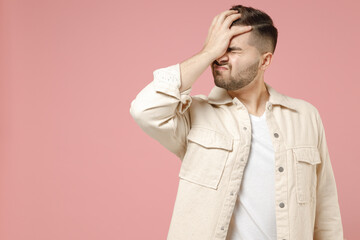 Young ashamed mistaken caucasian man 20s wearing jacket white t-shirt put hand on face facepalm epic fail gesture isolated on pastel pink color background studio portrait. People lifestyle concept