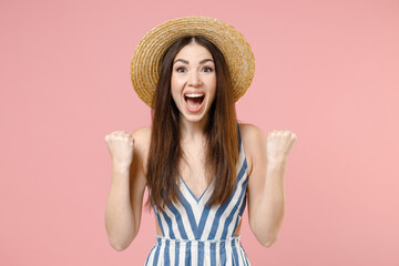 Young happy cheerful caucasian woman in summer clothes striped dress straw hat do winner gesture clench fist celebrating isolated on pastel pink background studio portrait. People lifestyle concept.