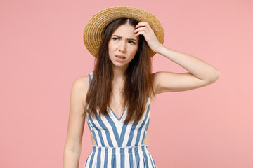 Young pensive sad puzzled troubled caucasian woman in summer clothes dress straw hat looking aside put hand on forehead isolated on pastel pink background studio portrait. People lifestyle concept