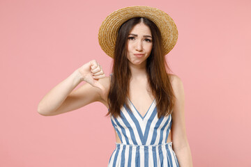 Young sad displeased dissatisfied caucasian woman in summer clothes striped dress straw hat show thumb down dislike gesture isolated on pastel pink background studio portrait People lifestyle concept