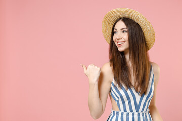 Young caucasian woman wear summer clothes striped dress straw hat point thumb finger back aside on copy space area mock up isolated on pastel pink background studio portrait. People lifestyle concept