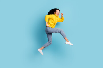 Fototapeta na wymiar Photo of excited lady jump run fast beaming smile look camera wear yellow sweater jeans shoes isolated blue background