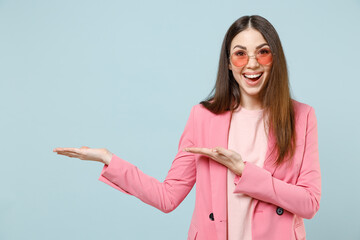 Young happy caucasian woman 20s in pastel pink clothes glasses pointing arms hands overhead on copy space area mock up workspace isolated on blue background studio portrait People lifestyle concept.