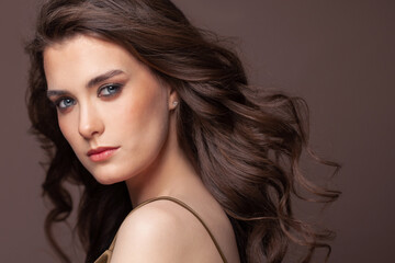 Naklejka premium Portrait of pretty young woman with blowing healthy curly hairdo and clear skin on brown background