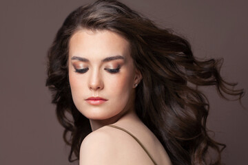 Naklejka premium Portrait of perfect young woman with blowing long perfect dark hair and clear skin on brown background