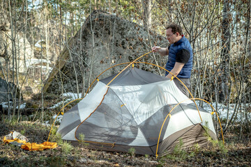 Male hiker is setting up a tent in the forest. Concept of tourism, hiking and staying in nature