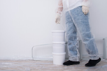 a man in protective clothing, brings buckets of paint and a set of tools, against the background of a white wall, there is a place for the inscription © kurgu128