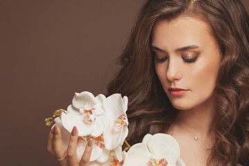 Healthy young model woman with perfect skin, brown curly hair and white orchid flowers. Facial treatment and skin care concept