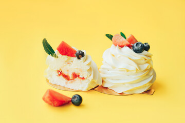 Delicious pastries covered with white and berries cream standing in row against yellow background