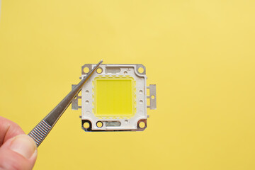 Led chip isolated on yellow background. Hand holding diode. Save energy concept.