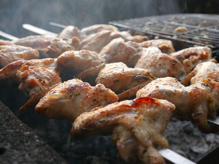 Chicken wings are fried on an open fire. There's smoke all around. Barbecue