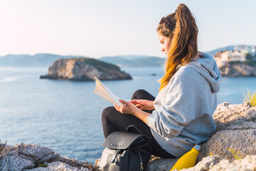 Caucasian woman reading a book on a cliff by the sea in the Malgrats Islands of Santa Ponça. Palma de Mallorca, Spain