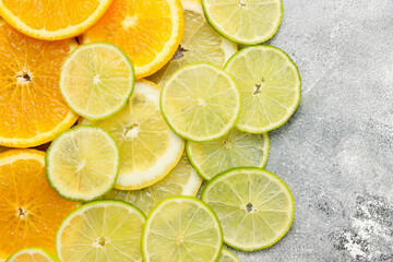 the background with cut citrus fruits of round form, sliced oranges, limes and lemons at at the grey beton background, copy space for text