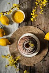 Homemade traditional lemon and pear bundt cake with lemons and forsythia on rustic table.