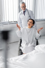 cheerful african american woman in wheelchair showing wow gesture near doctor, blurred foreground