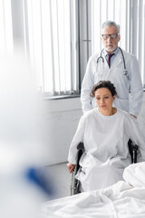 mature doctor near upset african american woman sitting in wheelchair, blurred foreground