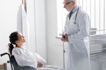 Obraz premium mature doctor talking to smiling african american woman sitting in wheelchair