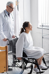 Obraz premium smiling doctor near happy african american woman sitting in wheelchair in hospital