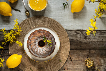 Homemade traditional lemon and pear bundt cake with lemons and forsythia on rustic table.