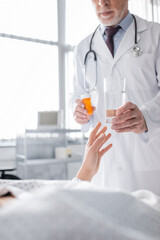 partial view of mature doctor giving water and medication to sick woman on blurred foreground