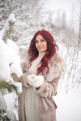 portrait of a young beautiful women with long red hair in winter forest of snowy park