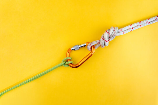 Orange carabiner. Equipment for climbing and mountaineering. Safety rope. Knot Prusik, clove hitch. Isolated on yellow background.
