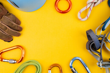 Climbing adventure equipment flat lay view. Top view of extreme mounteneering tools like helmet, carabiner, rope, gloves, radio, harness, figure eight. Concept on the trendy yellow background.