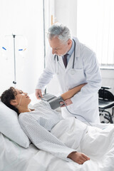 Obraz premium middle aged doctor going to measure blood pressure of african american woman in clinic