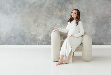 Perfect pregnant woman resting on white comfortable armchair on gray banner background with copy space