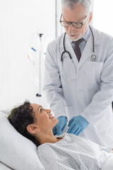 mature doctor in latex gloves examining shoulder of smiling african american woman in clinic