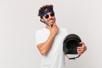 motorbike rider smiling with a happy, confident expression with hand on chin, wondering and looking...
