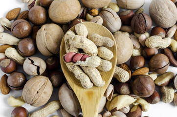 peanuts in the skin in a wooden spoon on the background of a scattering of different nuts, assorted nuts