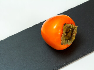 Ripe fresh persimmon fruit on stone cutting board.