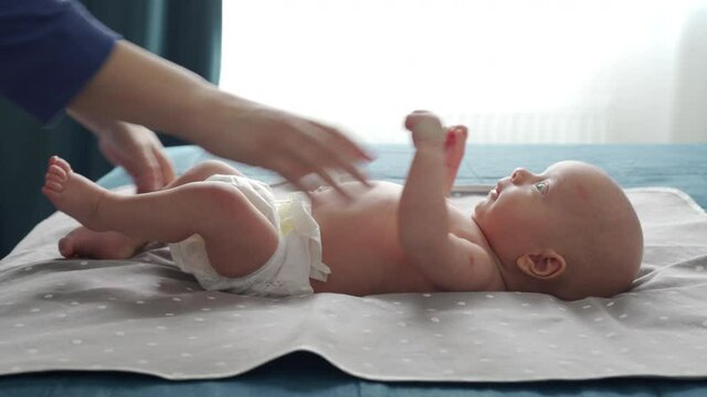 Mother with baby boy doing exercise simple exercises to make baby bones and muscles stronger, newborn infant lying on bed against the window. High quality 4k footage
