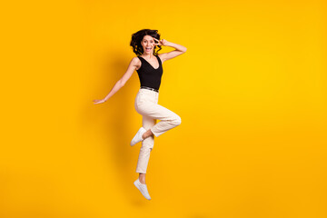 Fototapeta na wymiar Full length body size photo of funny woman jumping up showing v-sign gesture isolated on vibrant yellow color background