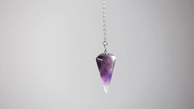 Purple Amethyst crystal pendulum hanging on chain on white background.
