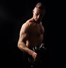 Fototapeta na wymiar Handsome strong sporty man doing the exercises with dumbbells on dark black shadow background. Closeup